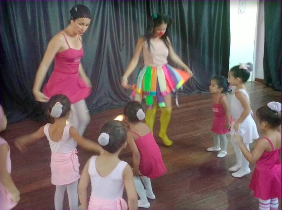Professoras conduzem uma atividade de dança com crianças em uma sala de madeira.